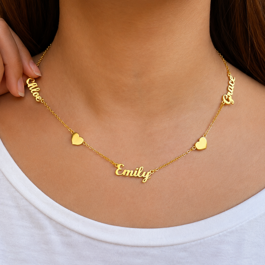 Gold name necklace with heart charms on a person wearing a white shirt