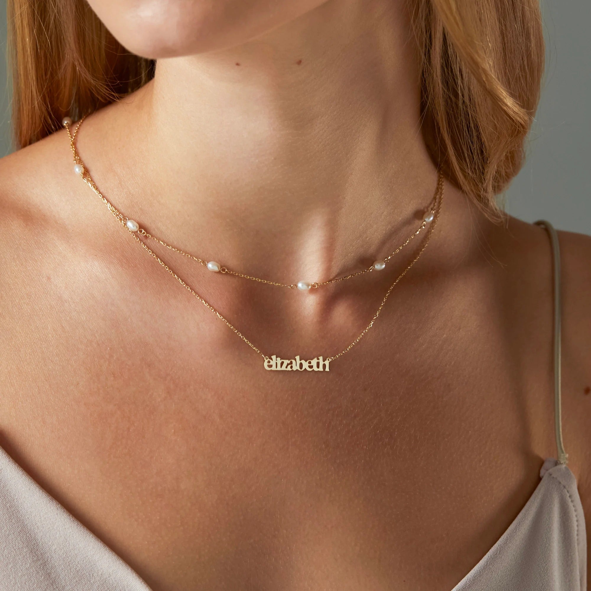 Gold necklace with 'Elizabeth' pendant on a person wearing a white top.