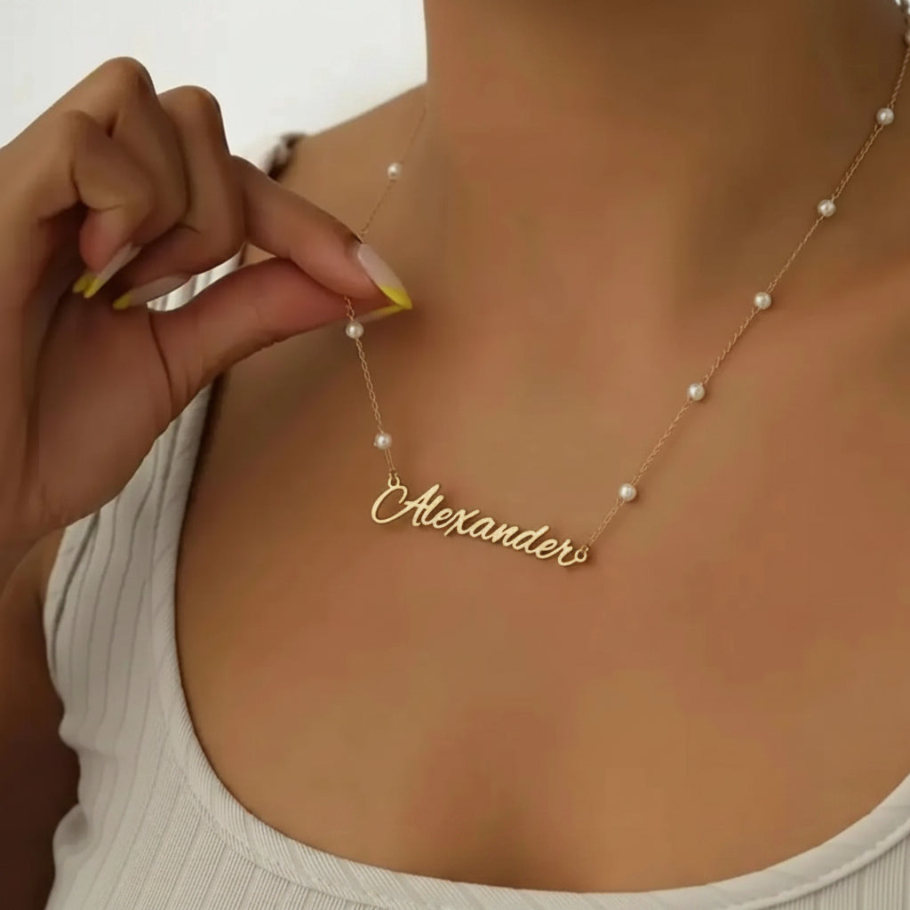 Gold necklace with 'Alexander' pendant on a person wearing a white top.