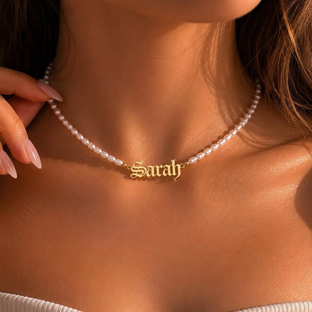 Gold necklace with 'Sarah' pendant on a person wearing a white top.